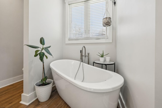 bathroom featuring baseboards, a freestanding bath, and wood finished floors