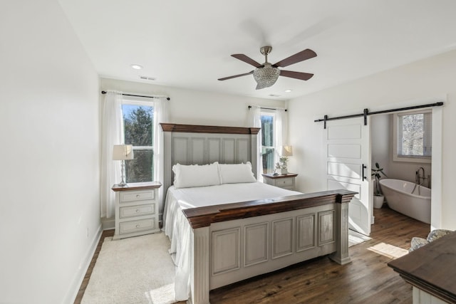 bedroom with visible vents, baseboards, a barn door, recessed lighting, and wood finished floors