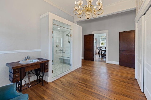 bathroom featuring wood-type flooring, an inviting chandelier, a shower with shower door, and sink