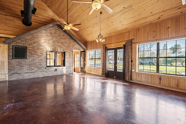 unfurnished living room with high vaulted ceiling, ceiling fan with notable chandelier, wooden walls, concrete flooring, and brick wall