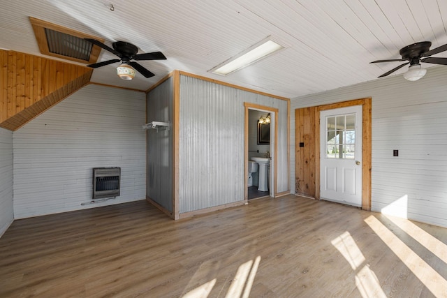 unfurnished living room featuring light wood-type flooring, wood ceiling, heating unit, ceiling fan, and wooden walls