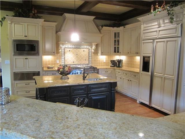 kitchen with decorative light fixtures, built in appliances, custom exhaust hood, and light stone countertops