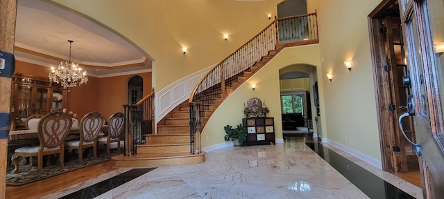 entryway featuring ornamental molding, a high ceiling, a chandelier, and a tray ceiling