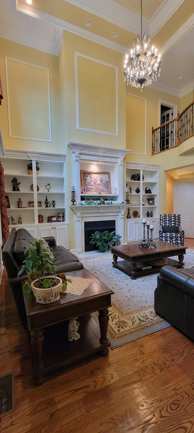 living room with built in shelves, hardwood / wood-style flooring, crown molding, and a chandelier