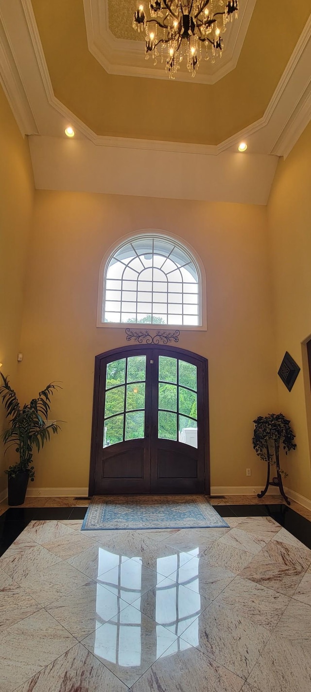 entrance foyer with a towering ceiling, french doors, ornamental molding, and a tray ceiling