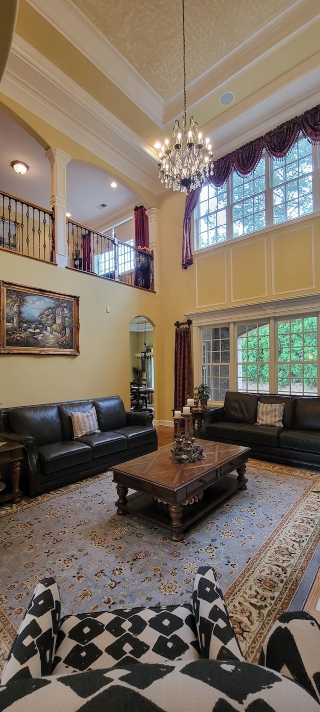 living room with a high ceiling, a textured ceiling, a notable chandelier, and crown molding