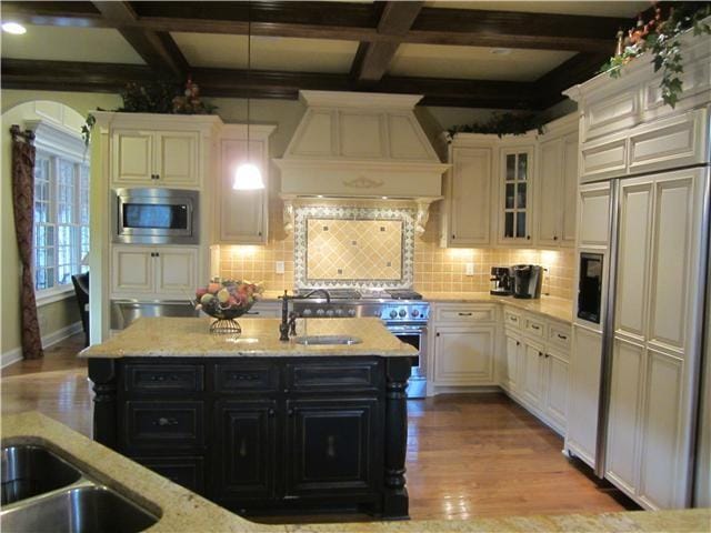 kitchen featuring custom exhaust hood, a kitchen island with sink, built in appliances, light hardwood / wood-style flooring, and decorative light fixtures