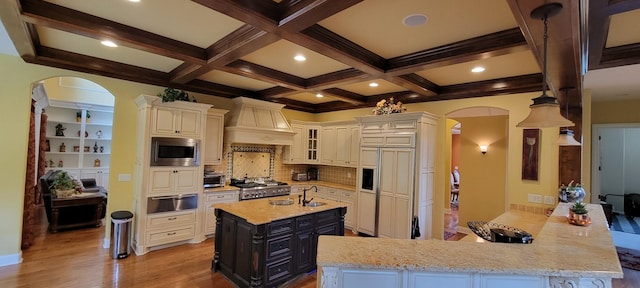 kitchen featuring beam ceiling, custom exhaust hood, built in appliances, and kitchen peninsula