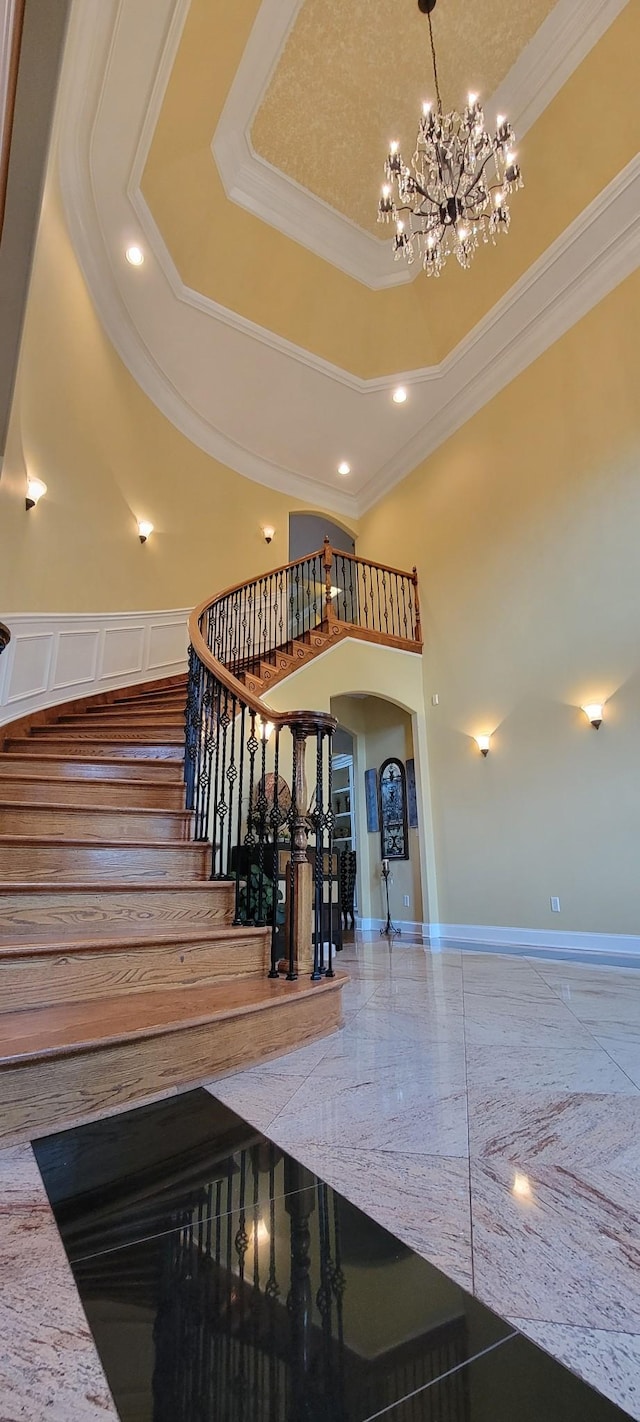 staircase featuring ornamental molding, an inviting chandelier, a high ceiling, and a tray ceiling