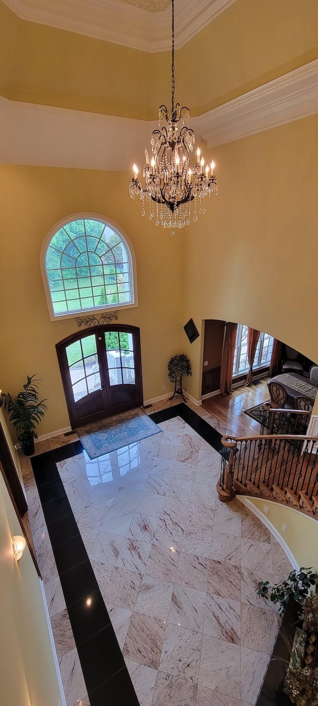 foyer entrance featuring a towering ceiling, ornamental molding, an inviting chandelier, and french doors