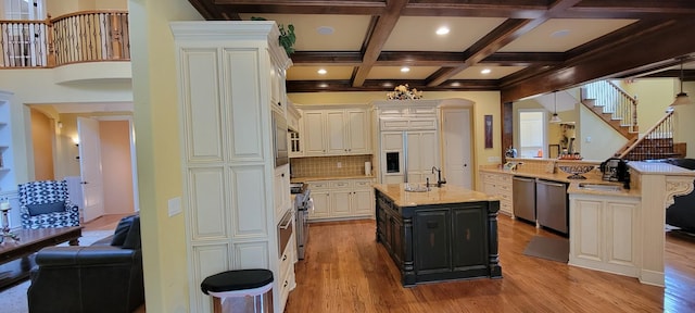 kitchen featuring beamed ceiling, an island with sink, light wood-type flooring, and decorative backsplash