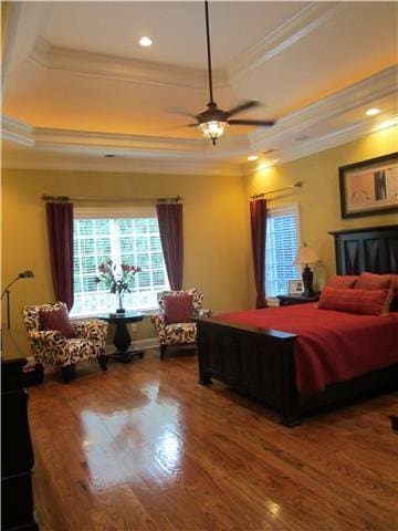 bedroom with ornamental molding, ceiling fan, a tray ceiling, and wood-type flooring