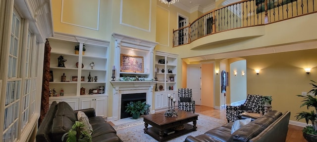 living room with a high ceiling, crown molding, light wood-type flooring, and built in features