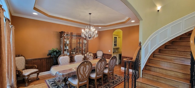 dining space with a raised ceiling, ornamental molding, and light wood-type flooring