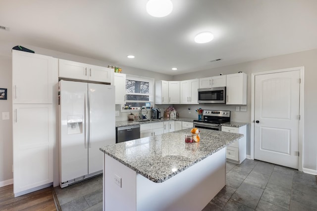 kitchen featuring a center island, sink, appliances with stainless steel finishes, light stone counters, and white cabinetry