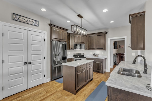 kitchen featuring appliances with stainless steel finishes, dark brown cabinetry, sink, decorative light fixtures, and light hardwood / wood-style floors