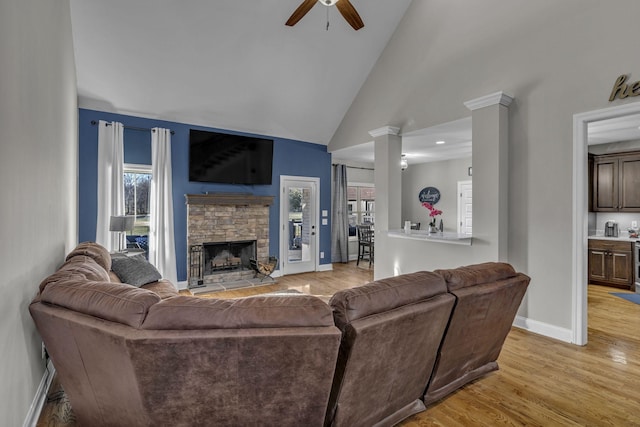 living room featuring high vaulted ceiling, light hardwood / wood-style flooring, ceiling fan, a fireplace, and decorative columns