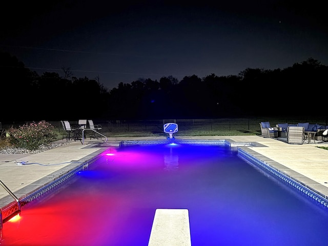 pool at night with an outdoor hangout area, a diving board, and a patio area