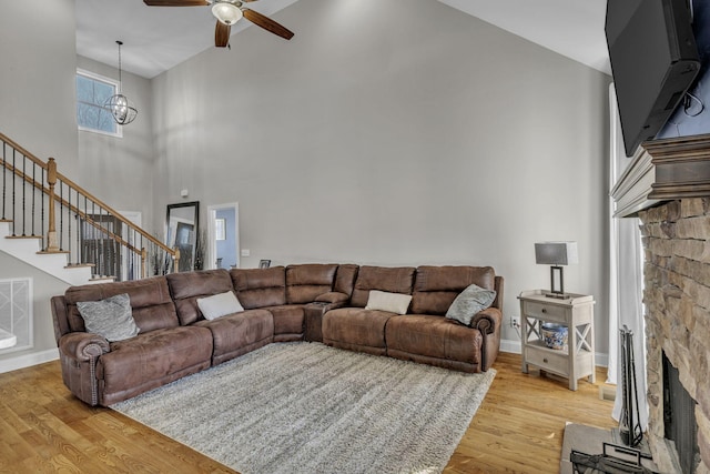 living room with ceiling fan, a fireplace, a towering ceiling, and light wood-type flooring