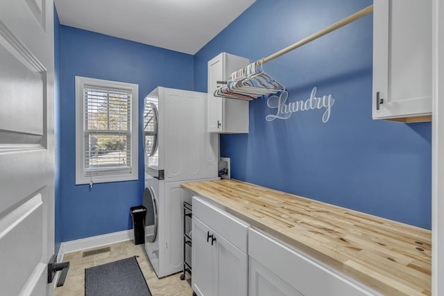 clothes washing area featuring light tile patterned flooring, cabinets, and stacked washing maching and dryer