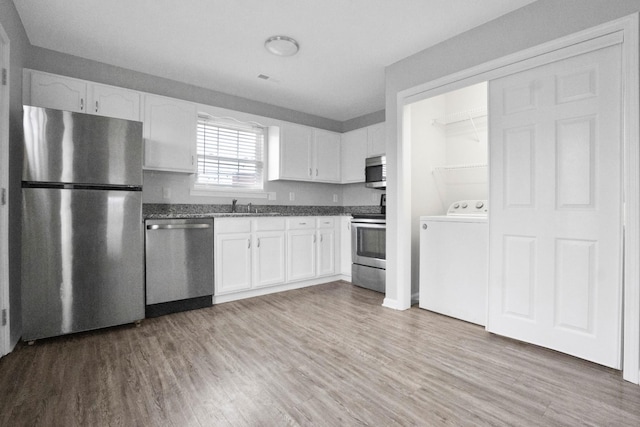 kitchen featuring appliances with stainless steel finishes, sink, wood-type flooring, white cabinets, and washer / clothes dryer