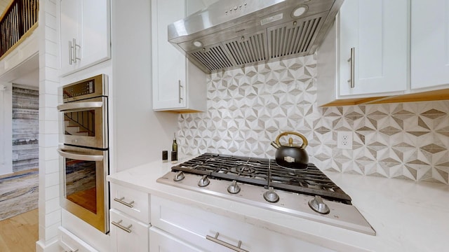 kitchen featuring backsplash, custom range hood, light stone counters, white cabinetry, and stainless steel appliances