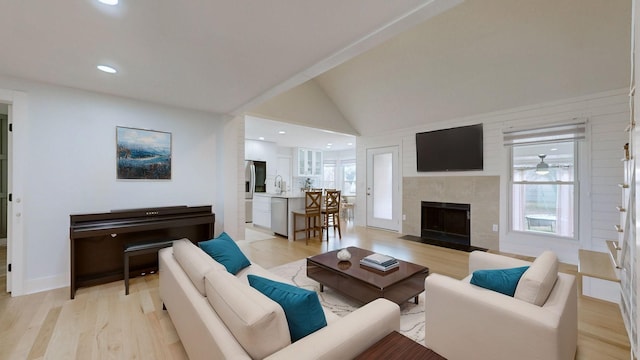 living room featuring sink, a fireplace, lofted ceiling, and light wood-type flooring