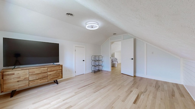 additional living space featuring a textured ceiling, vaulted ceiling, and light wood-type flooring