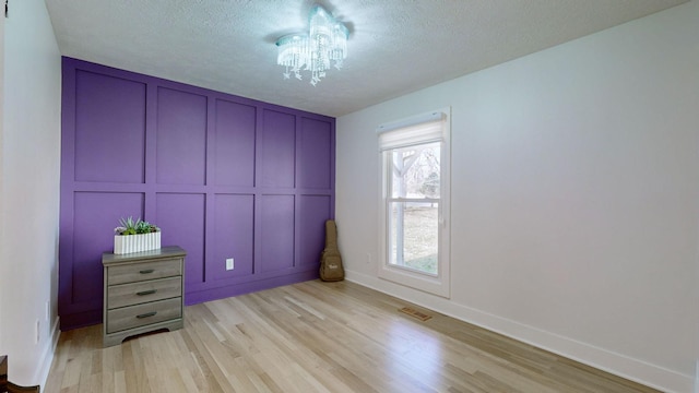 unfurnished bedroom with a notable chandelier, light wood-type flooring, and a textured ceiling