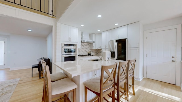 kitchen with decorative backsplash, light wood-type flooring, stainless steel appliances, sink, and white cabinetry