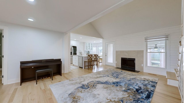 living room with a tile fireplace, sink, light hardwood / wood-style floors, and lofted ceiling