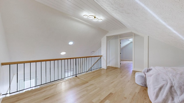 additional living space with a textured ceiling, vaulted ceiling, and light wood-type flooring