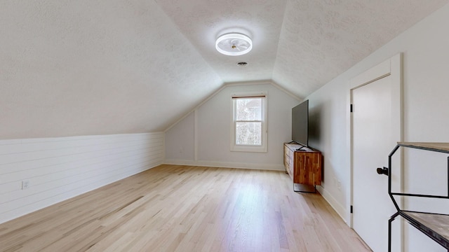 bonus room featuring vaulted ceiling, a textured ceiling, and light hardwood / wood-style flooring