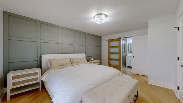 bedroom featuring a barn door, light hardwood / wood-style flooring, and ensuite bath