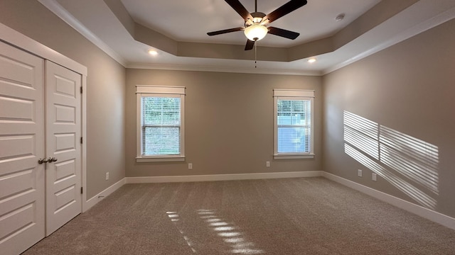 carpeted empty room with a tray ceiling, plenty of natural light, and ornamental molding