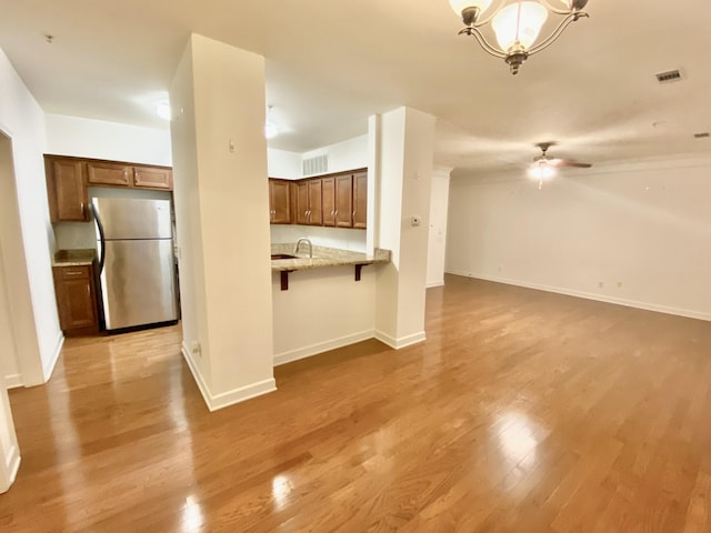 kitchen with a kitchen bar, stainless steel fridge, kitchen peninsula, light stone counters, and light hardwood / wood-style flooring