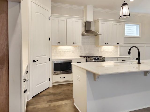 kitchen featuring appliances with stainless steel finishes, wall chimney exhaust hood, sink, decorative light fixtures, and white cabinets