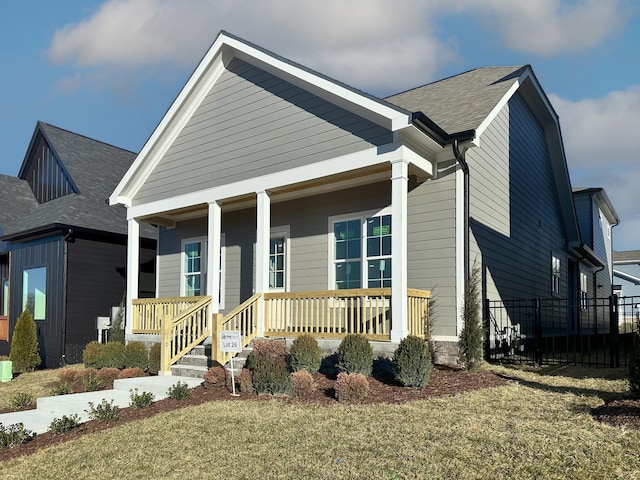 view of front of home featuring a porch, a front yard, roof with shingles, and fence