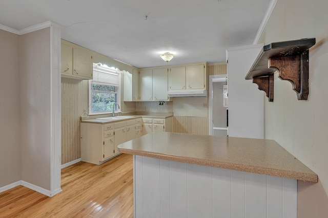 kitchen with kitchen peninsula, ornamental molding, sink, cream cabinetry, and light hardwood / wood-style floors