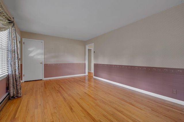 empty room with baseboard heating, a healthy amount of sunlight, and light wood-type flooring