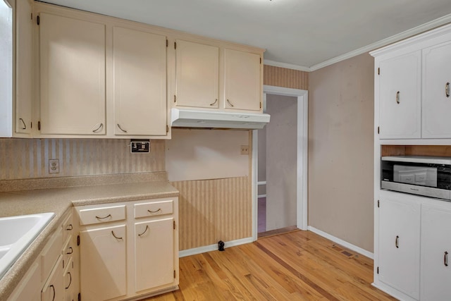 kitchen with light wood-type flooring, built in microwave, ornamental molding, and sink