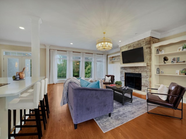 living room featuring built in shelves, crown molding, hardwood / wood-style flooring, a notable chandelier, and a fireplace