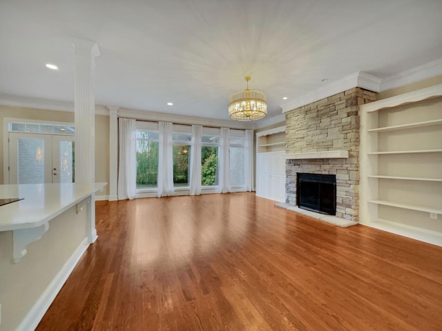 unfurnished living room with built in shelves, a stone fireplace, a notable chandelier, crown molding, and wood-type flooring