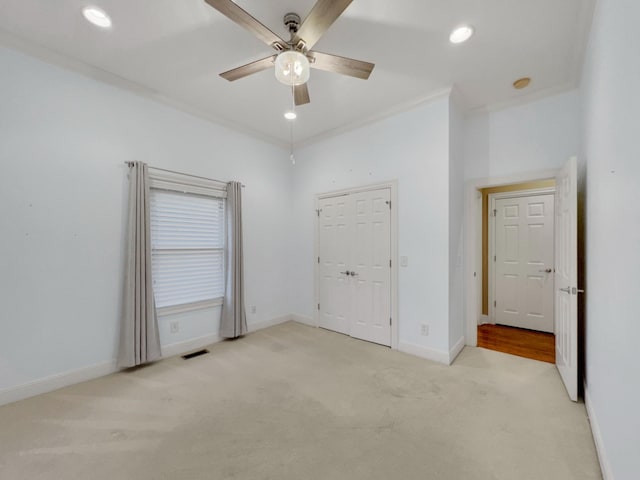 unfurnished bedroom with a closet, light colored carpet, ceiling fan, and ornamental molding