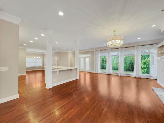 unfurnished living room featuring a chandelier, hardwood / wood-style flooring, plenty of natural light, and crown molding