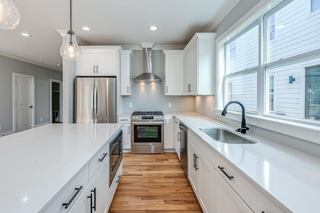 kitchen with white cabinetry, sink, wall chimney exhaust hood, hanging light fixtures, and stainless steel appliances