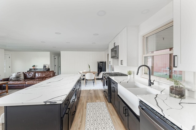 kitchen featuring light hardwood / wood-style flooring, appliances with stainless steel finishes, white cabinetry, a center island, and light stone countertops