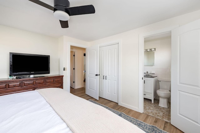 bedroom featuring connected bathroom, sink, tile walls, light hardwood / wood-style flooring, and a closet