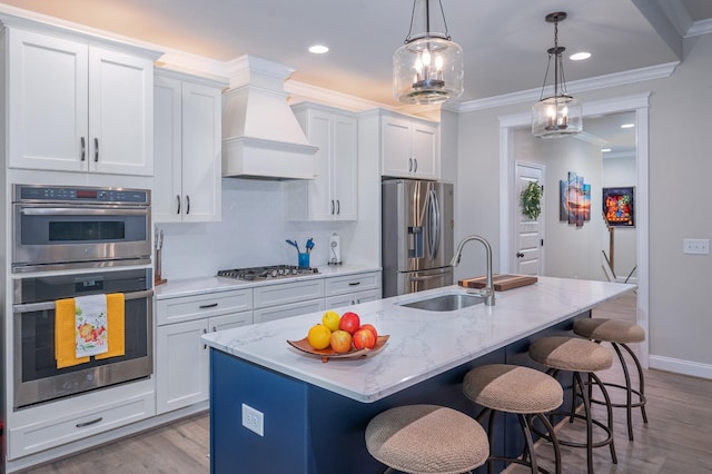 kitchen with light stone counters, stainless steel appliances, pendant lighting, white cabinetry, and an island with sink