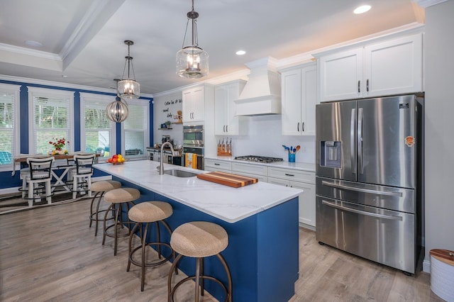 kitchen with a kitchen island with sink, hanging light fixtures, custom range hood, appliances with stainless steel finishes, and white cabinetry